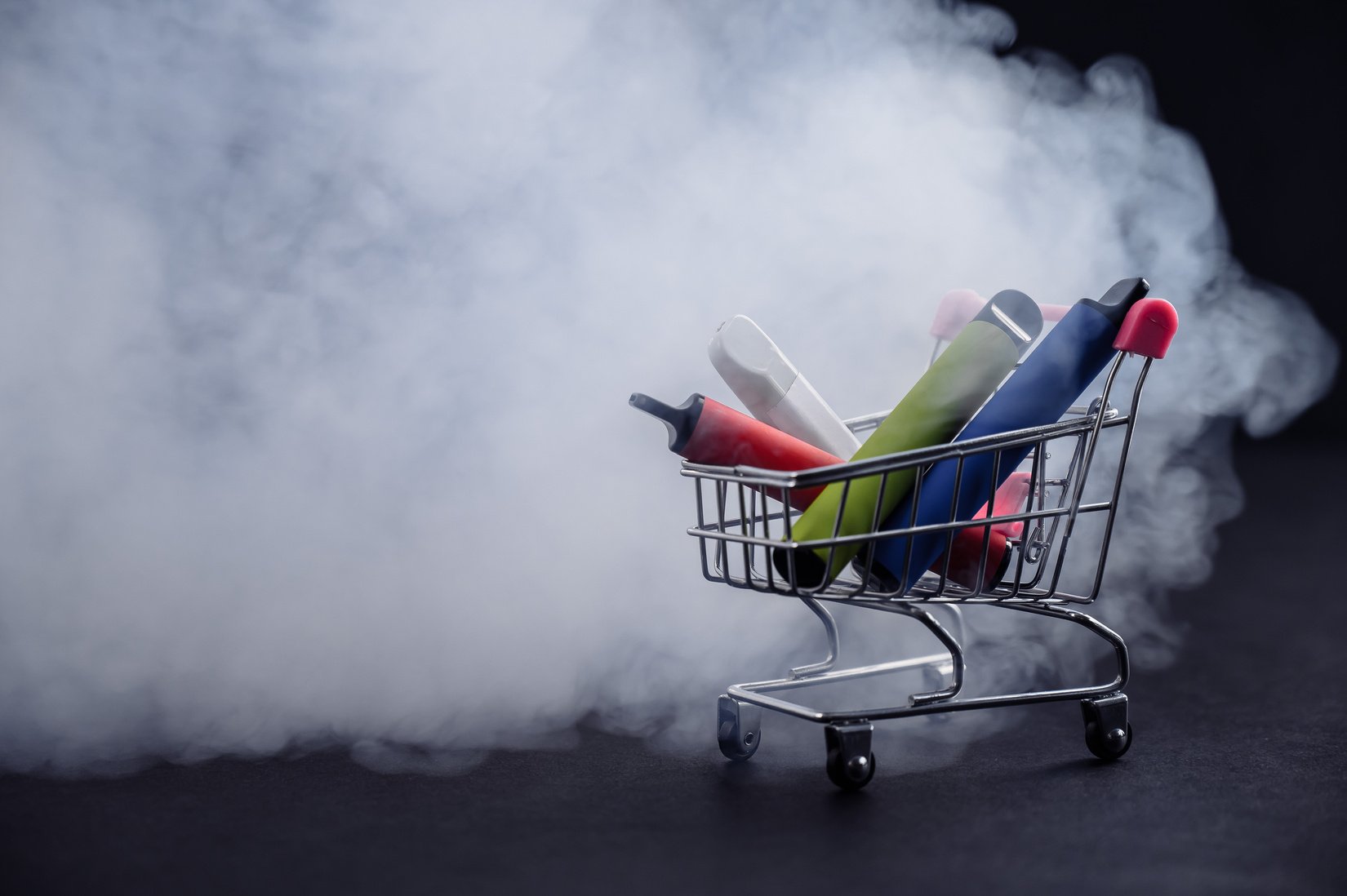 Disposable Vapes in a Shopping Cart on a Black Background. Modern Electronic Cigarettes.